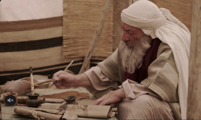 Moses sitting at a low table writing the Torah