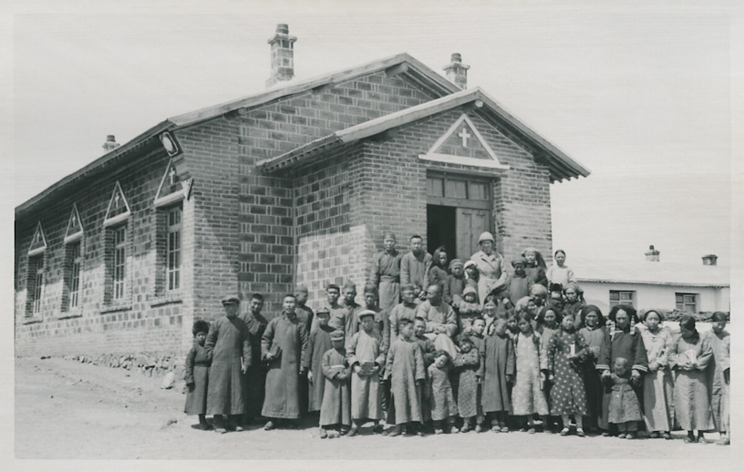 Crowd of people in front of a small masonry church building