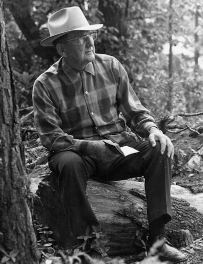 Townsend seated on a log next to a tree holding an open book