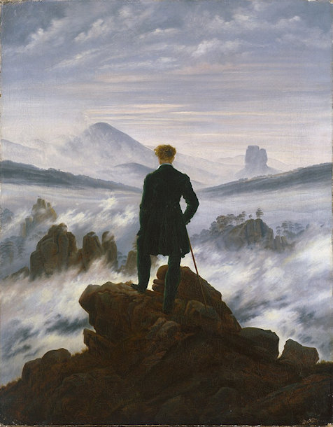 Man standing on a mountaintop looking toward distant peaks emerging from fog