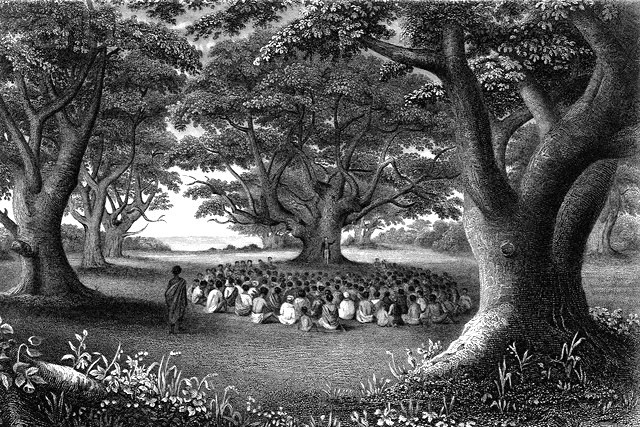 Missionary preaching to a crowd seated under kukui trees