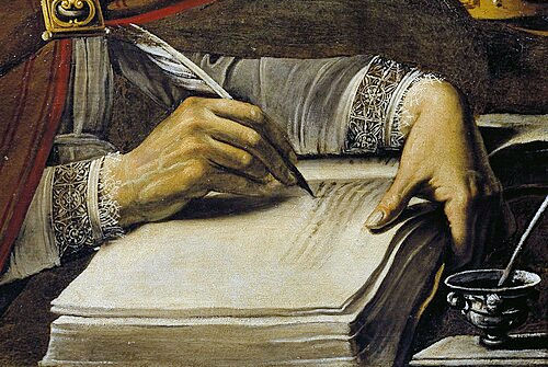 Detail of a hand writing with a quill in an open book