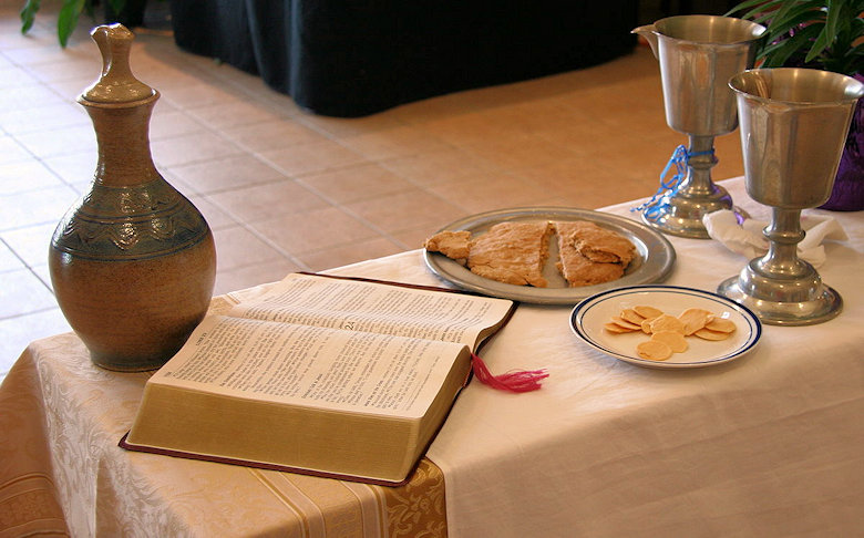 Communion table with an open Bible, two plates with pieces of bread and two drinking cups